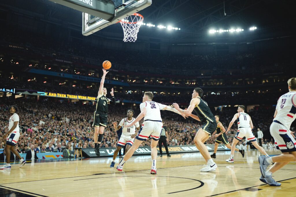 Un giocatore di basket dei Purdue Boilermakers, a mezz'aria, tira a canestro durante una partita sullo sfondo di un'arena gremita.