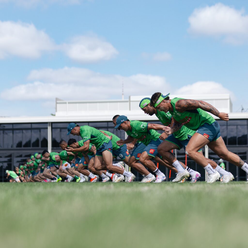 Skupina hráčů Canberra Raiders v zelených dresech sprintuje během tréninku za slunečného dne.